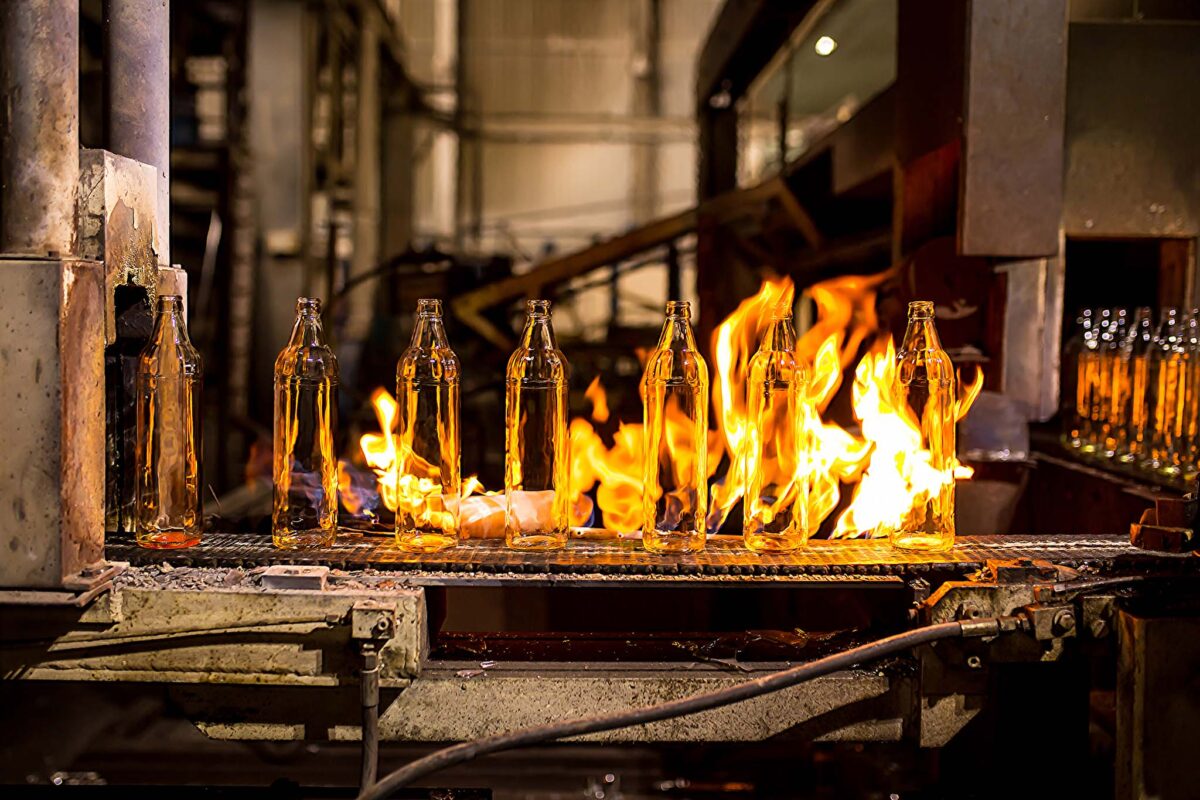 Glass factory, industrial production of glass containers. Modern technology, robots machines make products.Party bottles for drinks. Technological work at the plant. Working atmosphere with copy space